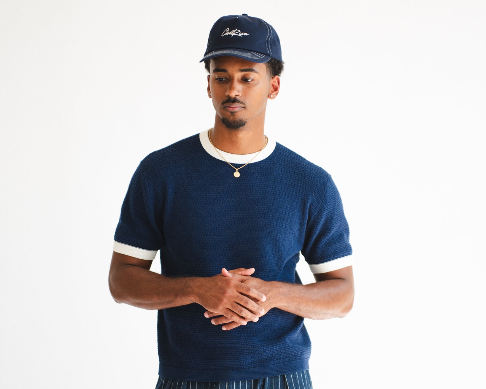 Man wearing a navy blue sweater with white trim and striped pants on a white background